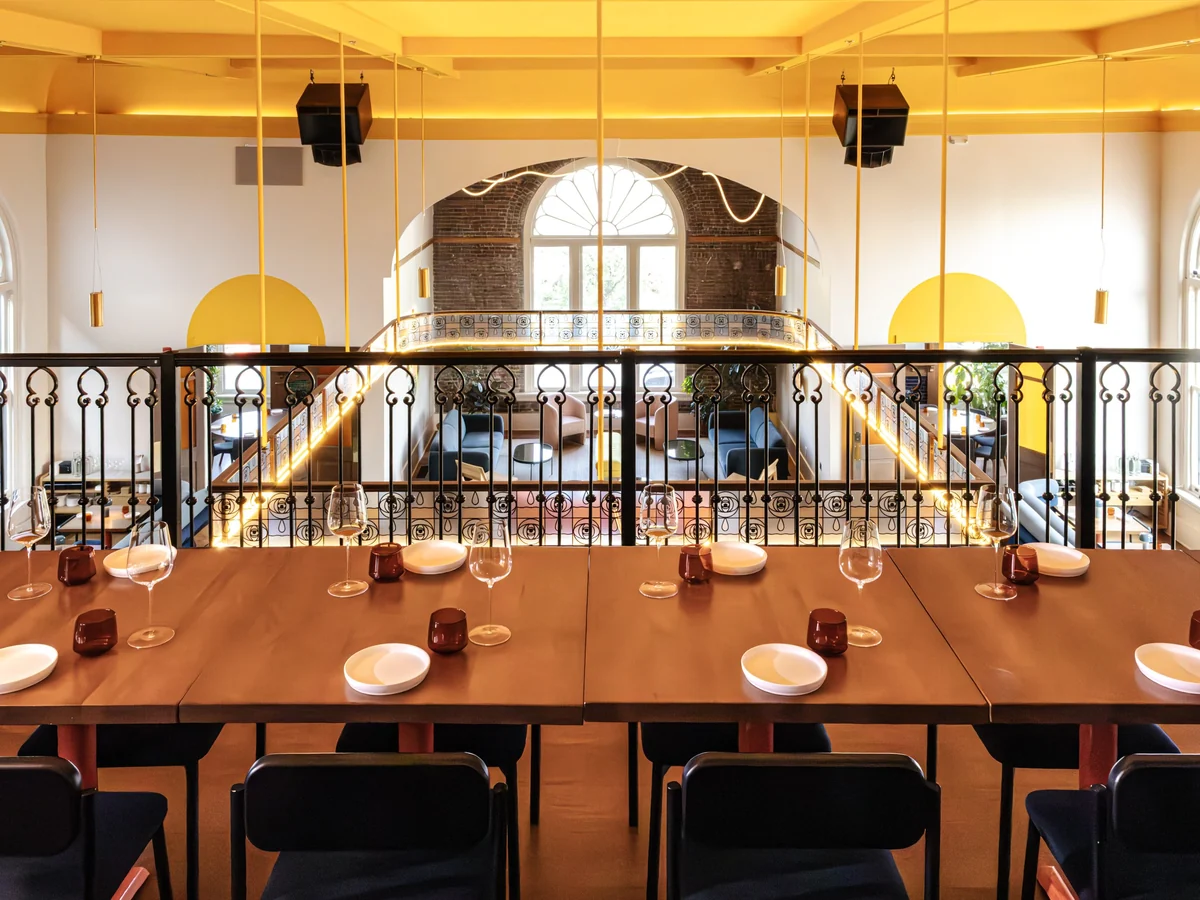Bad Idea’s mezzanine tables look toward an arched church window below yellow ceiling beams.