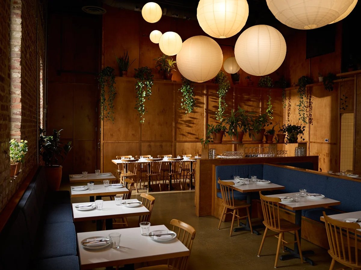 Folk’s dining room with round paper lanterns, wood tables, blue banquettes, and hanging greenery.